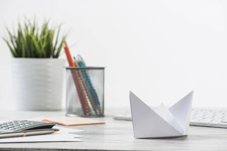 Wooden office desk with white origami boat. Professional invest strategy and direction. Flat lay office workplace with green plant in pot, computer keyboard and calculator. Individual opportunityの写真素材