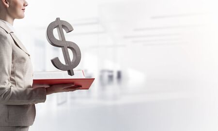 Businesswoman with dollar sign above opened notebook. Investment and money saving services. Elegant young woman in white business suit on blurred background. Financial company advertising.の写真素材