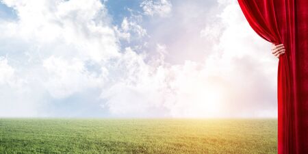 Human hand opens red velvet curtain to landscape with green grassの写真素材