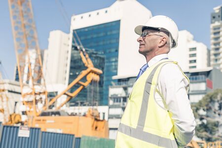 Engineer man in helmet and jacket controlling outdoor construction site