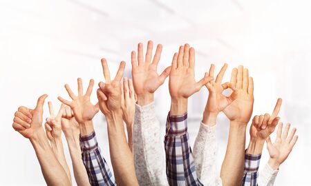 Row of man hands showing various gestures. Ok, finger pointing, victory, spread fingers, clenched fist and thumb up signs. Human hands gesturing on light blurred background. Many arms raised together.の写真素材
