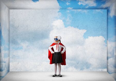Little confident child in mask and cape in empty room plays cool superhero. Mixed mediaの写真素材