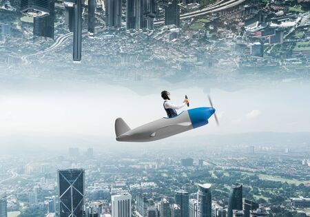 Young pilot sitting in cabin of small airplane. Abstract image of two modern urban worlds located...