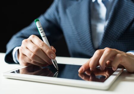 Man in business suit using tablet computer. Close-up of male hands holding pen and tablet gadget. Businessman at workplace in office. Mobile smart device in business occupation. Digital technologyの写真素材