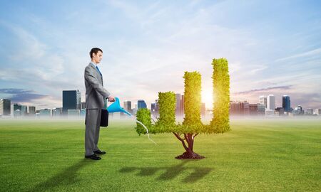 Businessman watering green plant in shape of financial graph at field. Business analytics and statistics. Friendly ecosystem for business and investment. Business growth and development.の写真素材