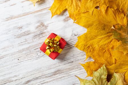 Bright autumn composition with gift box and yellow maple leaves. Holiday present decorated golden ribbon bow lies on vintage wooden desk. Happy thanksgiving congratulation. Autumn sale advertising.の写真素材