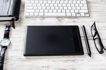 Top view office workspace composition. Flat lay wooden desk with pc keyboard, glasses, watch and graphic tablet. Design and creativity. Time management and planning. Designer workplace organizationの写真素材