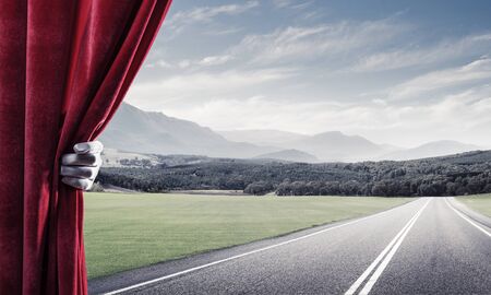 Human hand in glove opens red velvet curtain to landscapeの写真素材