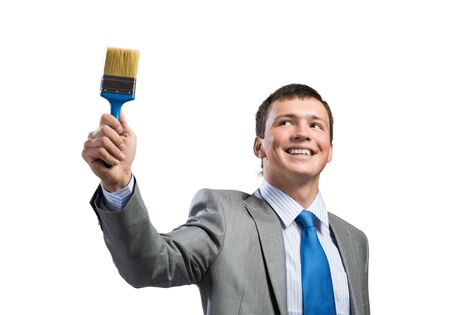 Smiling creative businessman painter holding paintbrush in hand. Portrait of joyful handsome man in business suit and tie isolated on white background. Ambitions and creativity in business concept.の写真素材