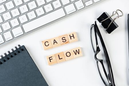 Cash flow statement concept with letters on wooden cubes. Still life of office workplace with supplies. Flat lay white surface with computer keyboard and notepad. Budget planning, audit and accountingの写真素材