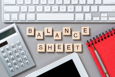 Balance sheet concept with letters on wooden cubes. Still life of office workplace with supplies. Flat lay grey surface with tablet computer and calculator. Budget planning, audit and accounting.の写真素材