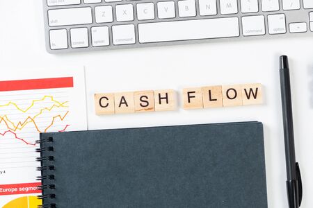 Cash flow statement concept with letters on wooden cubes. Still life of office workplace with supplies. Flat lay white surface with computer keyboard and notepad. Budget planning, audit and accountingの写真素材