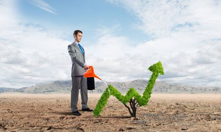 Businessman watering green plant in shape of of grow up trend in desert. Business analytics and statistics. Friendly ecosystem for business and investment. Business growth and development.の写真素材