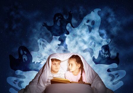 Cute girl and boy reading kids book in bed. Children with flashlight lying under blanket together....