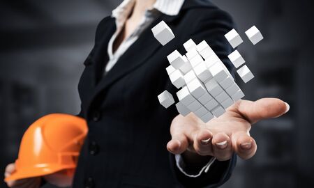Businesswoman holds in palm abstract 3d cube model. Woman engineer in business suit with orange...