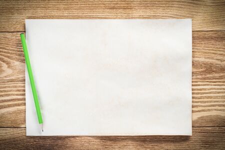 Sheet of paper lying on wooden table. Scrapbooking and hand made creativity. Rectangular blank white paper with pencil. Textured natural wooden background. View from above with copy space.の写真素材