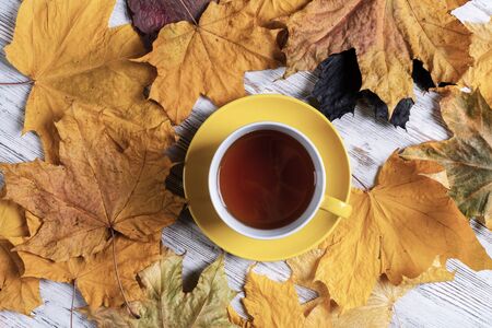 Flat lay autumn composition with cup of black tea and yellow autumn leaves. Time of tea break concept. Hot beverage lies on vintage wooden desk with bright foliage. Still life of morning tea ceremony.の写真素材