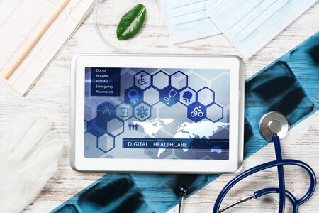 Modern social health insurance program. Tablet computer with healthcare application interface on screen. Stethoscope, x-ray image and cardiogram on wooden desk. Digital healthcare technologies.の写真素材