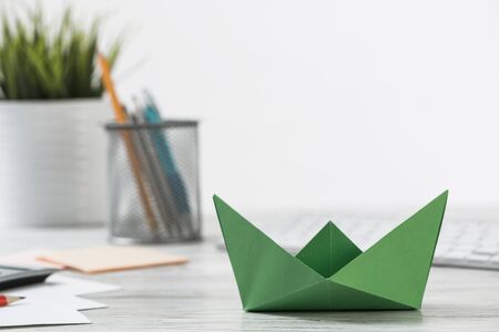 Wooden office desk with green origami boat. Green technologies and innovations. Flat lay office workplace with plant in pot, computer keyboard and calculator. Leadership development conceptの写真素材