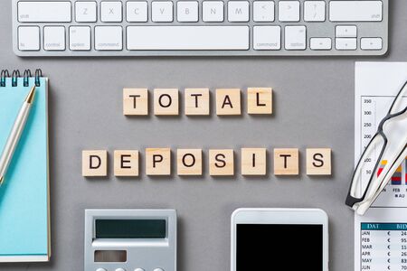 Total deposits concept with letters on wooden cubes. Still life of office workplace with supplies. Flat lay grey surface with keyboard and smartphone and calculator. Capital savings and banking.の写真素材