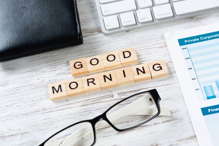 Good morning message with letters on wooden cubes. Still life of workspace with supplies. Flat lay wooden desk with computer keyboard and spiral notebook. Morning greeting phrase and motivation.の写真素材