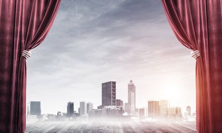 Human hand opens red velvet curtain to modern cityscape and cloudy skyの写真素材