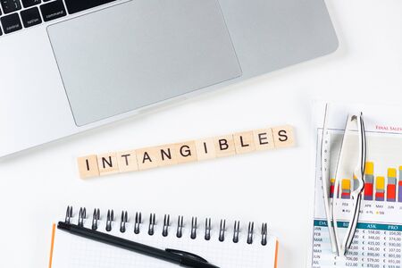 Intangibles concept with letters on wooden cubes. Still life of office workplace with supplies. Flat...