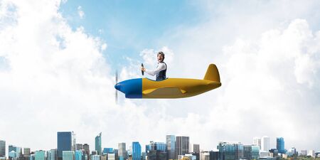 Businessman in aviator hat and goggles driving propeller plane above downtown with high modern...