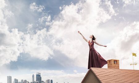 Young attractive woman on brick house roof stretching hand to sky.の写真素材