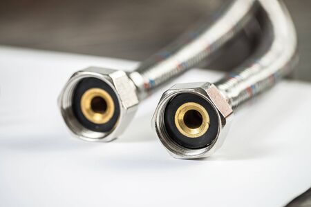 Water braided metal hose with connecting internal screw. Close up flexible hydraulic system. Plumbing pipeline laying on table. New equipment for bathroom repair or construction service.の写真素材