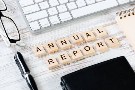 Annual report concept with letters on cubes. Still life of office workplace with supplies. Flat lay vintage wooden desk with computer keyboard and leather wallet. Company development and analyticsの写真素材