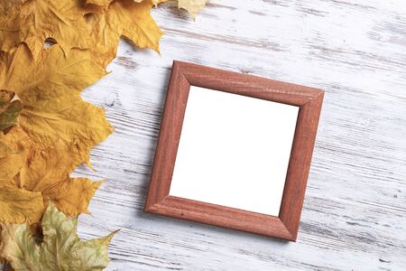 Blank rectangular photo frame lies on vintage wooden desk with bright autumn foliage. Flat lay with...
