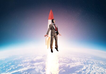 Business person in suit launching upwards on rocket. Progress and innovation technology. Corporate employee flying with jetpack rocket in stratosphere. Leadership motivation and goal achievement.の写真素材