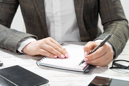 Close up woman hand holding pen. Businesswoman writing in notepad. Female secretary working at desk. Corporate woman in suit at her workplace in office. Business person doing notes on paper.の写真素材