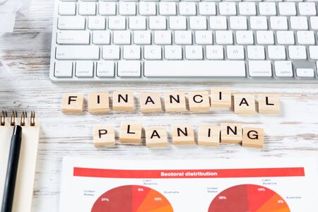 Financial planning concept with letters on cubes. Still life of office workplace. Flat lay vintage wooden desk with computer keyboard and analytic report. Company development and consulting analysis.の写真素材