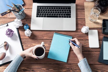 Woman writing in notebook with pen at desk. Online business education. Flat lay office workplace with female hands and laptop. Digital technology and coworking space. Female journalist taking notesの写真素材