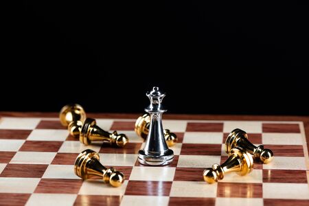 Silver queen chess defeats gold pawns on wooden chessboard. Intellectual duel and tactical battle in...