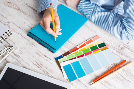 Top view creative designer working at vintage wooden desk. Office workplace with tablet computer and office accessories. Business occupation and creativity. Close up female hand writing in notepad.の写真素材