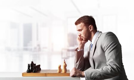 Businessman moving chess figure in chessboard. Successful management and leadership concept. Handsome man in business suit sitting at desk with chess. Operative tactics and strategy planningの写真素材