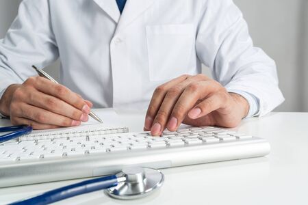 Doctor typing on wireless computer keyboard in office. Physician in white medical gown works with computer at desk. Professional diagnosis and treatment in modern hospital. Professional healthcareの写真素材