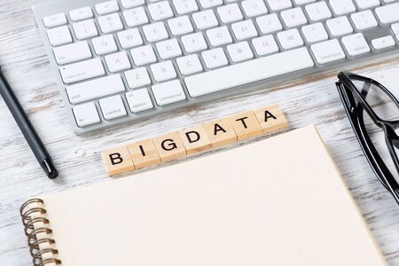 Big data analytics concept with letters on cubes. Still life of workplace with supplies. Flat lay vintage white wooden desk with computer keyboard and spiral notebook. Machine learning solution.の写真素材