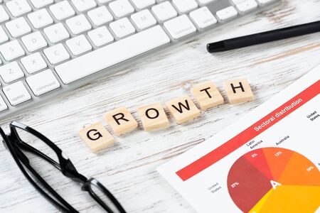 Financial growth concept with letters on cubes. Still life of office workplace with supplies. Flat lay vintage wooden desk with computer keyboard and analytic report. Investment strategy and analyticsの写真素材