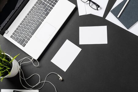 Top view of office workplace with digital gadgets. Flat lay black surface with laptop, green plant and white paper sheets. Top view coworking workspace with devices. Digital technology and mobility.の写真素材