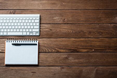 Top view of modern businessman workplace. Spiral notepad and computer keyboard on brown wooden surface. Education, creativity and innovation concept with copy space. Flat lay vintage office workspaceの写真素材