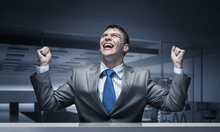 Happy excited businessman celebrating victory in business. Businessman feeling satisfaction from win. Portrait of guy wears business suit and tie in conference room. Personal success and triumphの写真素材