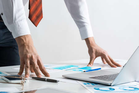 Businessman in suit and tie standing near office desk with documents and laptop. Meeting in...