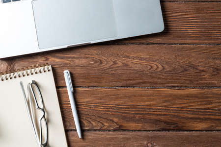 Top view of modern working place. Spiral notepad, pen and laptop computer on brown wooden surface. Education, creativity and innovation concept with copy space. Digital technology in modern business.の写真素材