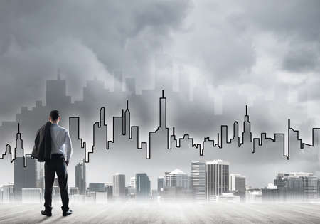 Businessman standing with back and looking at silhouette of modern business centerの写真素材