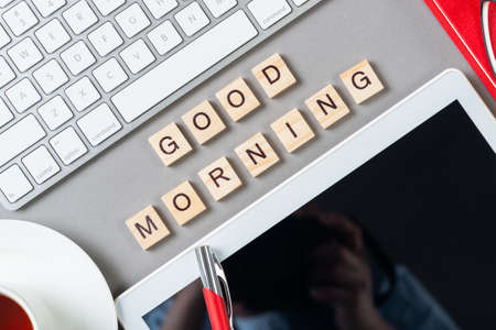 Good morning message with letters on wooden cubes. Still life of workspace with supplies. Flat lay grey surface with computer keyboard and cup of tea. Morning greeting phrase and motivation.の写真素材