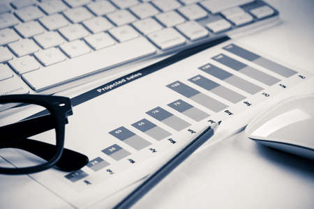 Business workplace with keyboard glasses and financial documents on tableの写真素材